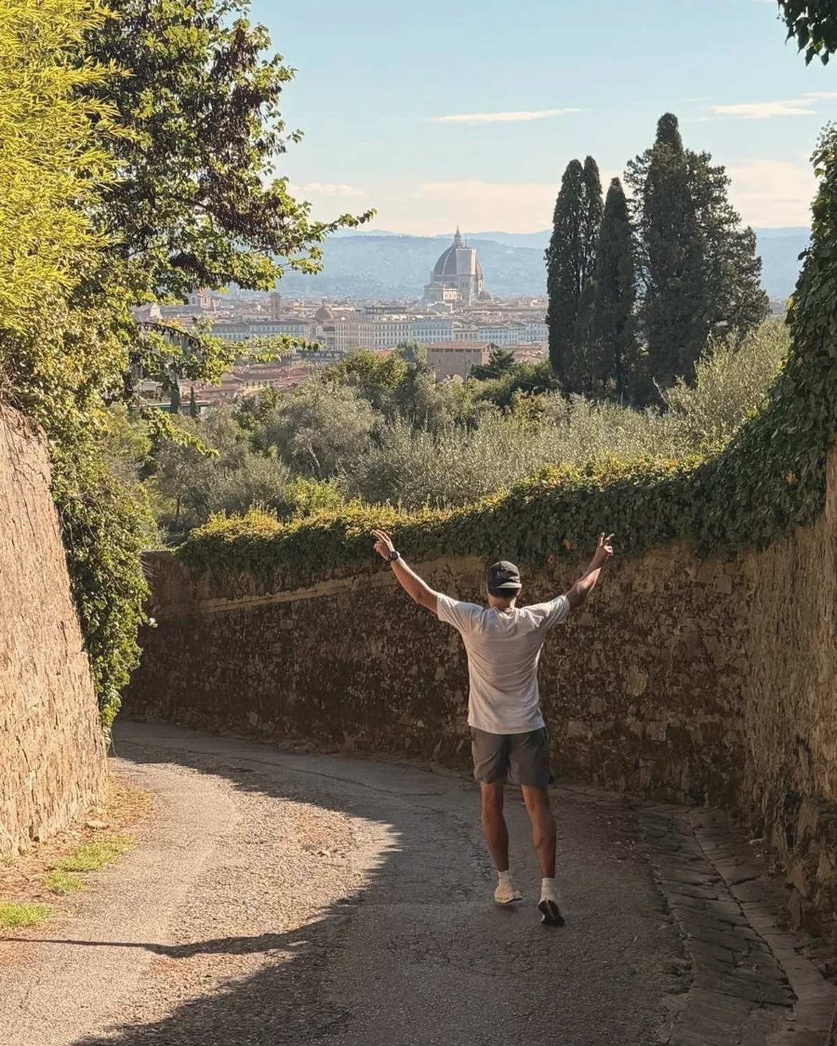 Ricardo mid-run on a walled lane above Florence, arms up, the Duomo in the distance