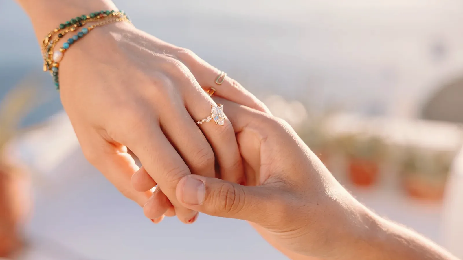 Elise's hand in Ricardo's, the engagement ring catching the Santorini light