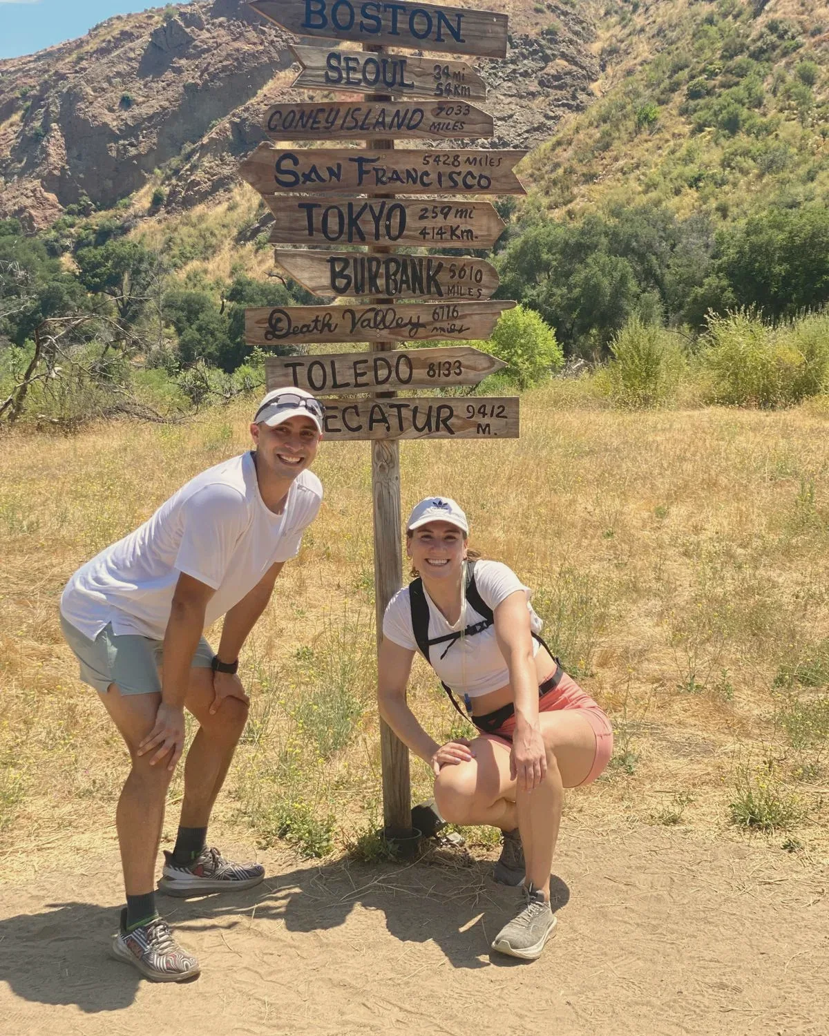 Elise and Ricardo posing under a hand-painted trail signpost that points to cities around the world