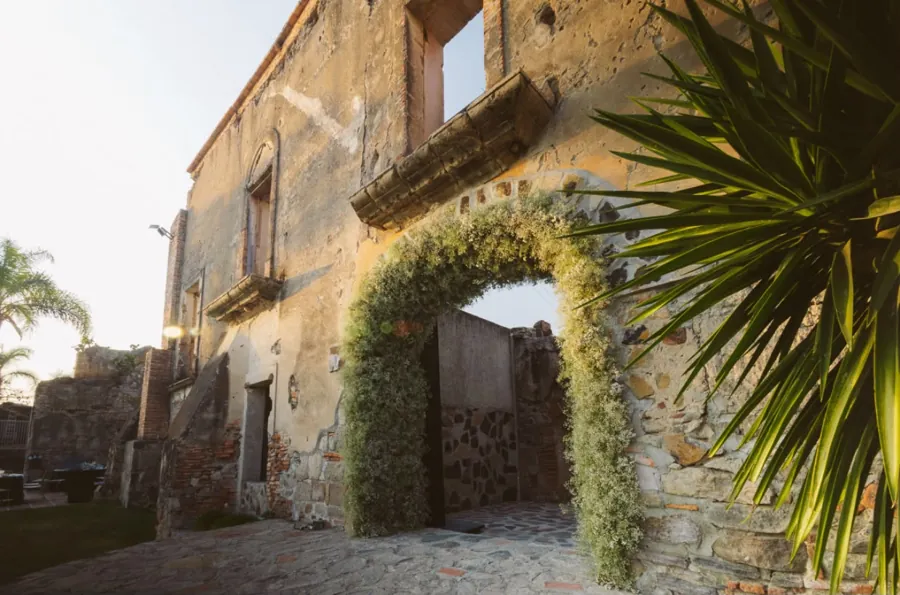 The stone entrance arch of Hacienda Concepci&oacute;n, greenery climbing the wall, a palm behind it