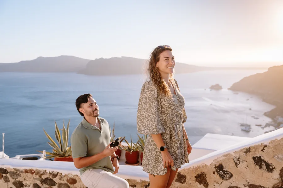 Elise and Ricardo standing at a stone terrace wall above the caldera, potted agaves between them