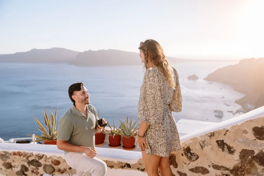 The two of them at the terrace wall, the caldera cliffs soft in the haze behind