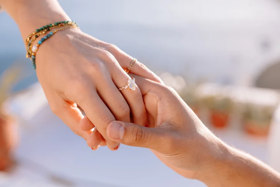 Close-up of Elise’s hand in Ricardo’s, the engagement ring on her finger, beaded bracelets on her wrist
