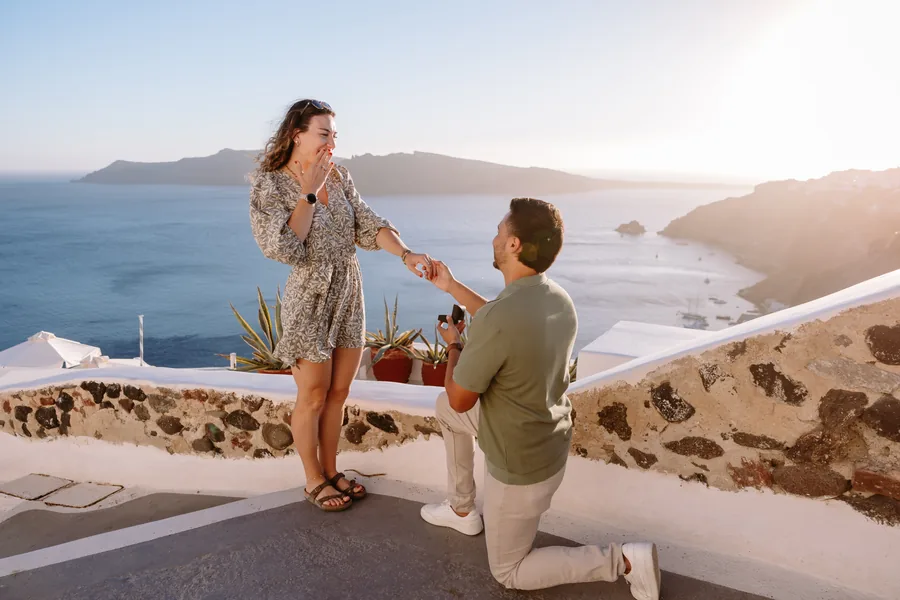 Ricardo on one knee, Elise laughing, the sea and the cliffs behind them