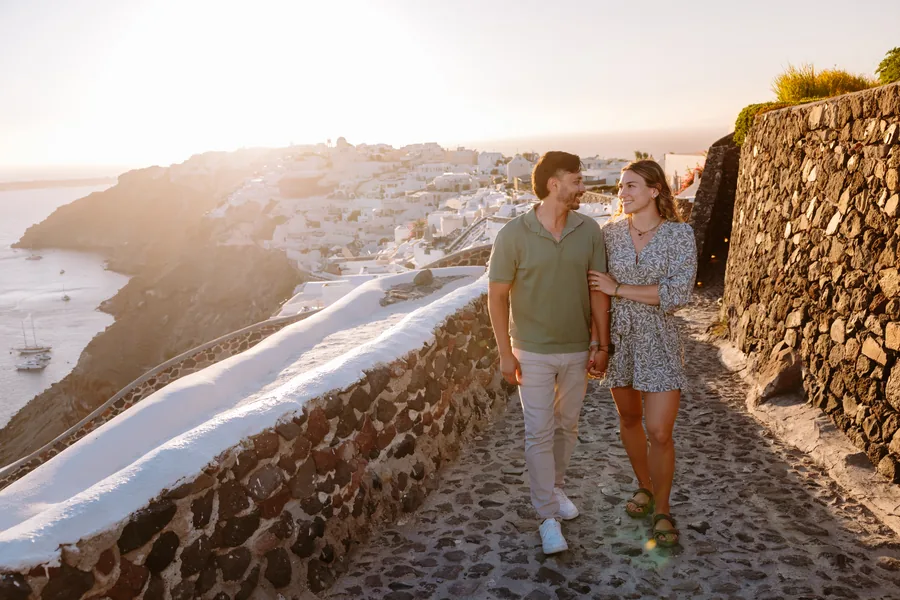 Walking along the stone-walled path, Oia’s white houses climbing the hill behind