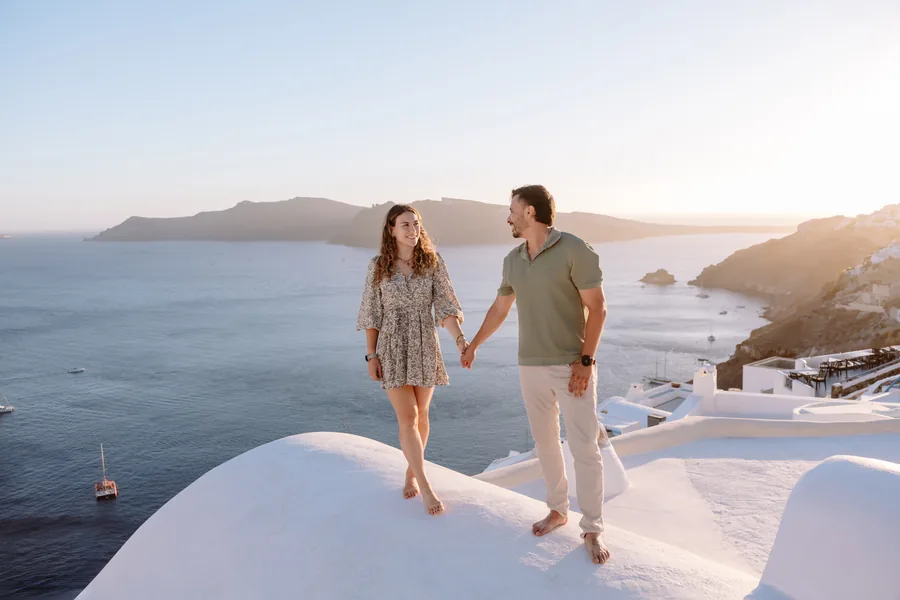 Elise and Ricardo walking hand in hand across a whitewashed dome, the caldera below