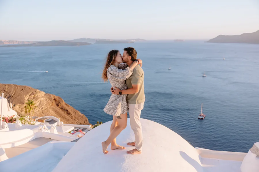 Ricardo lifting Elise on the dome, Oia’s rooftops behind