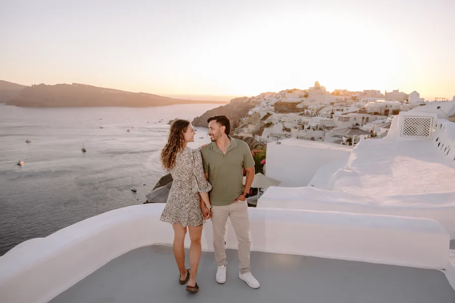 A white terrace above the bay, Elise and Ricardo holding hands, the island in the distance