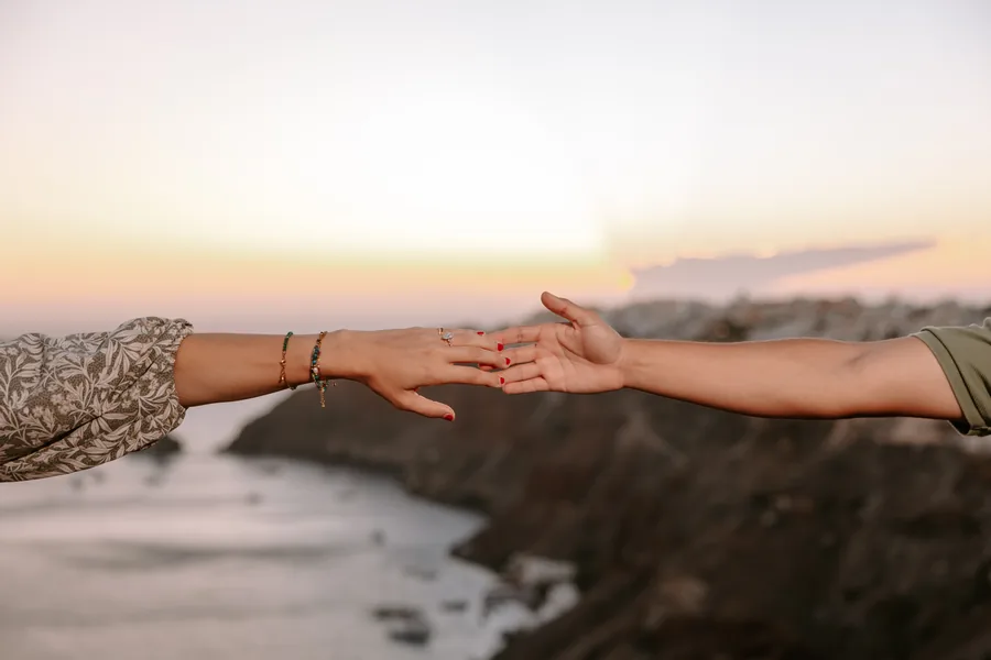 Two hands reaching for each other over the caldera at sunset