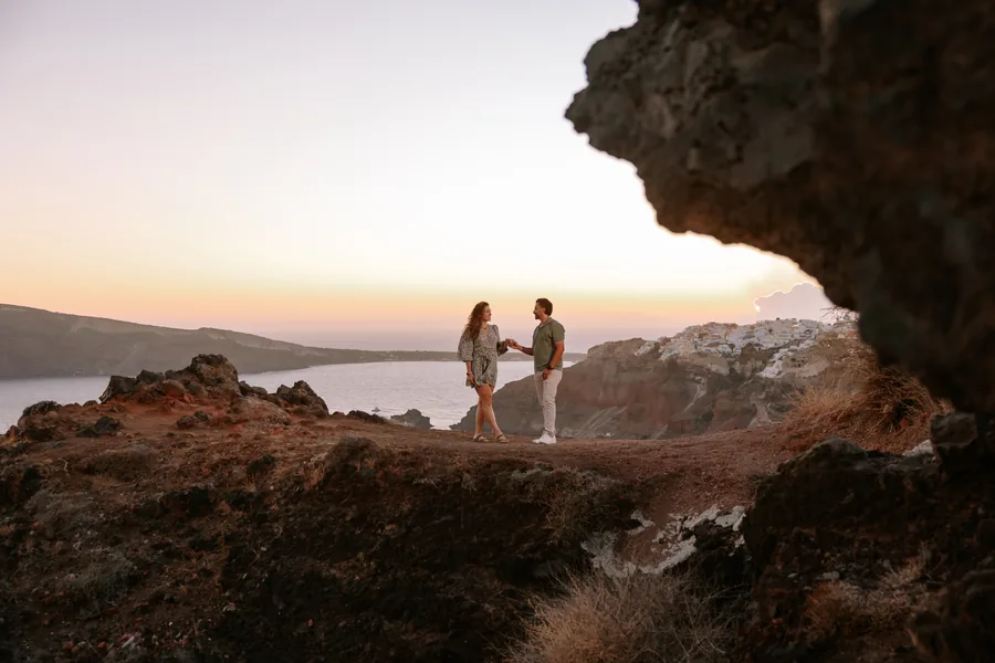 The two of them standing small on the cliff above Oia at sunset