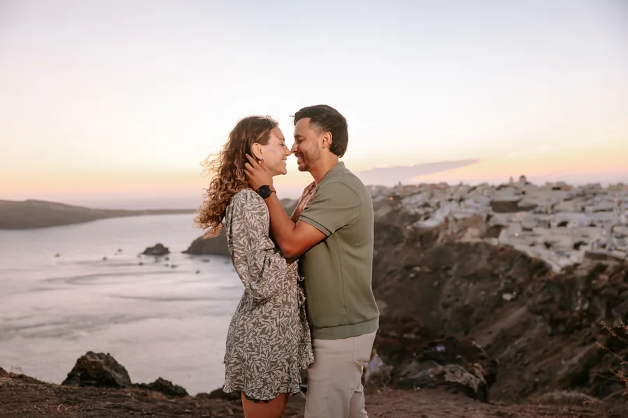 Elise and Ricardo holding each other on the cliff above Oia as the sun goes down