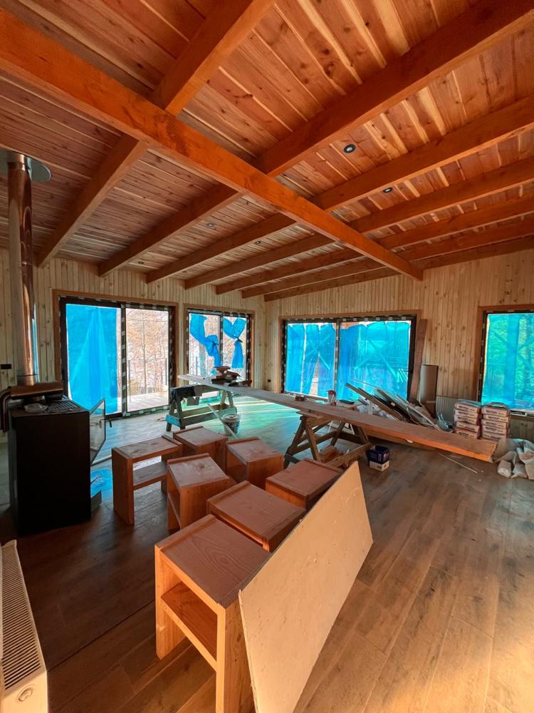 Living con cielo de madera y vigas a la vista, estufa a leña y ventanales