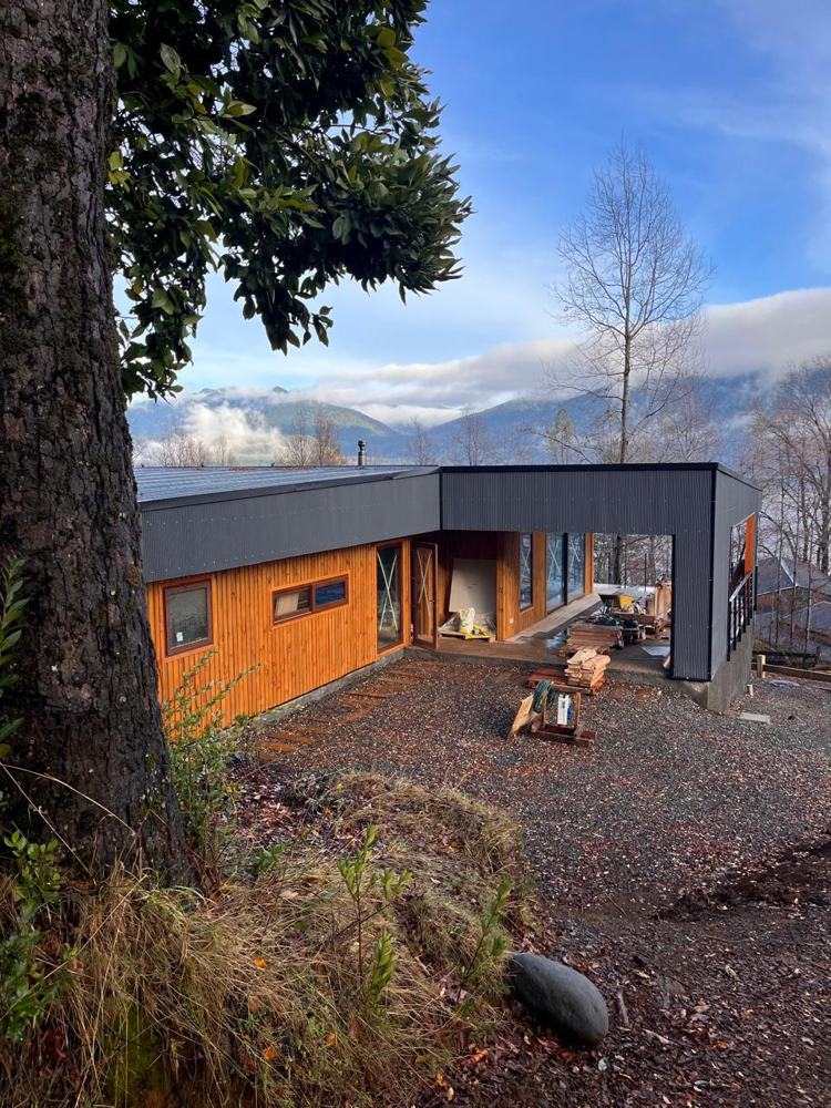 Casa en Caburgua con revestimiento de madera y techo metálico, cerros y nubes al fondo