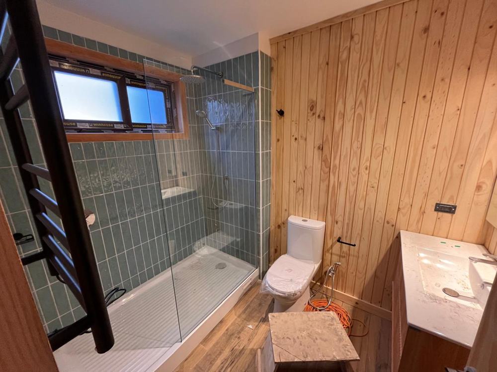 Baño con cerámica verde, muro de madera y ducha con vidrio