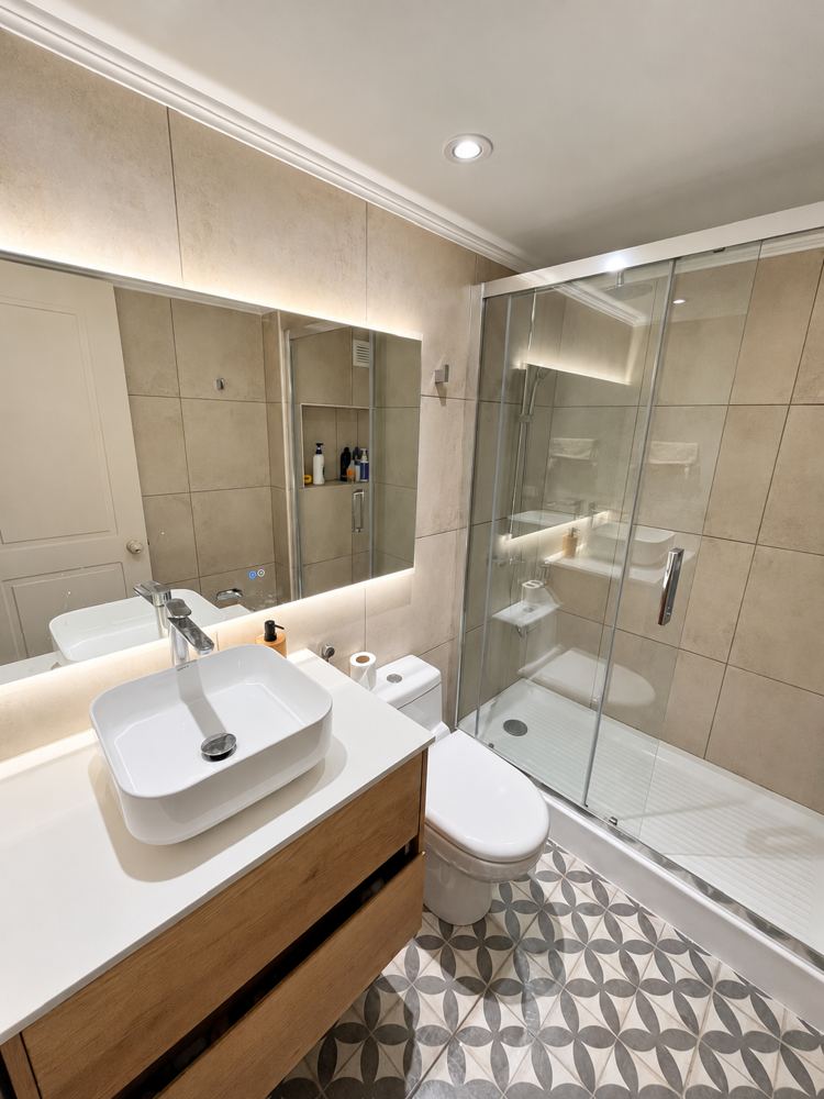 Baño remodelado con porcelanato gran formato, espejo retroiluminado y mueble de madera