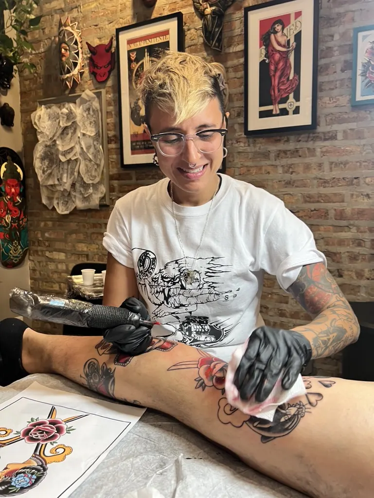 Orne smiling while tattooing a client's leg at Nowhereland Tattoo Studio
