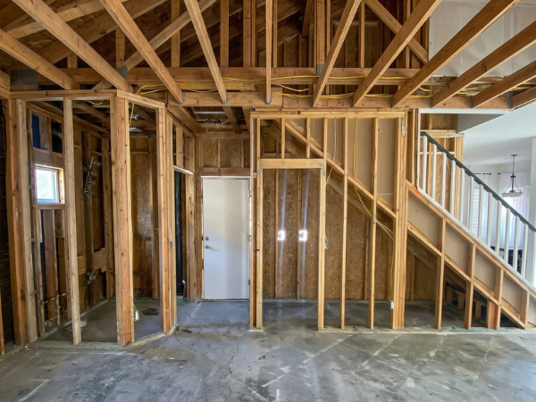 An unfinished basement with exposed wooden framing for walls and ceiling, a white door, and a partially built staircase.