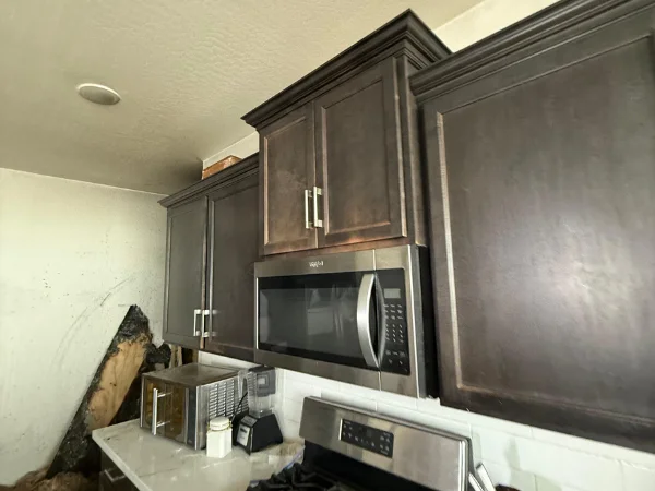 Kitchen cabinets and an oven over a counter with a microwave and a blender showing apparent fire damage.