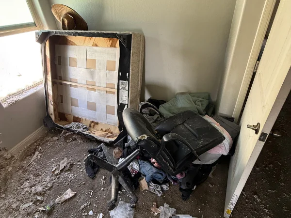 A chaotic room with an overturned sofa, a broken office chair, and piles of clothes, indicating a state of disarray.