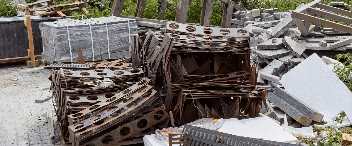A cluttered view of construction waste, including rusty metal sheets, wrapped paving stones, and rubble on a dirt ground. A cluttered view of construction waste, including rusty metal sheets, wrapped paving stones, and rubble on a dirt ground.