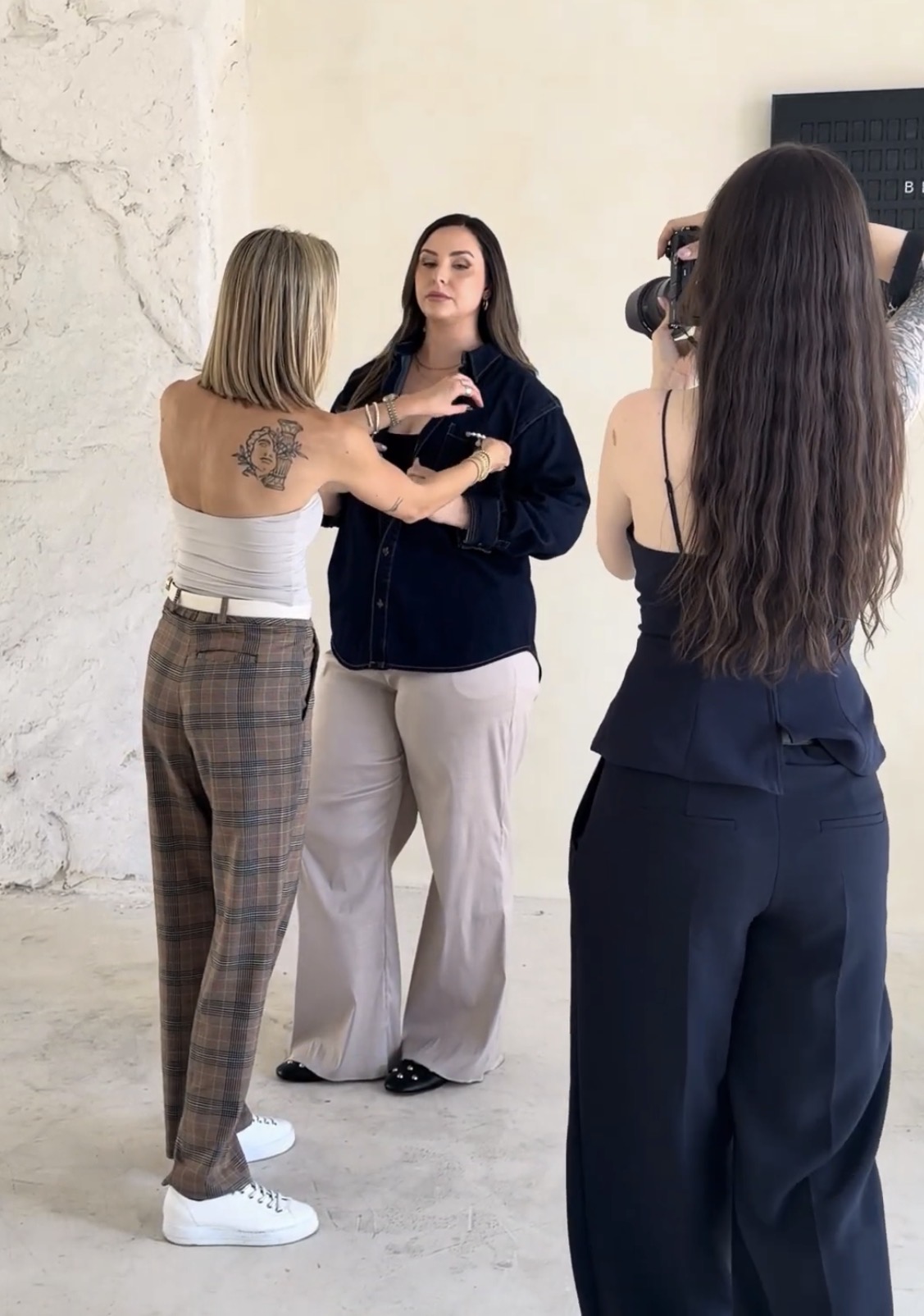 Maggie adjusting a client’s denim shirt on set while a photographer prepares the shot