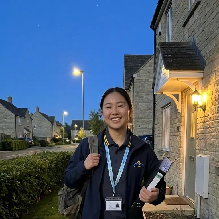 A smiling carer with a lanyard and folder on a Cotswold-stone street at dusk