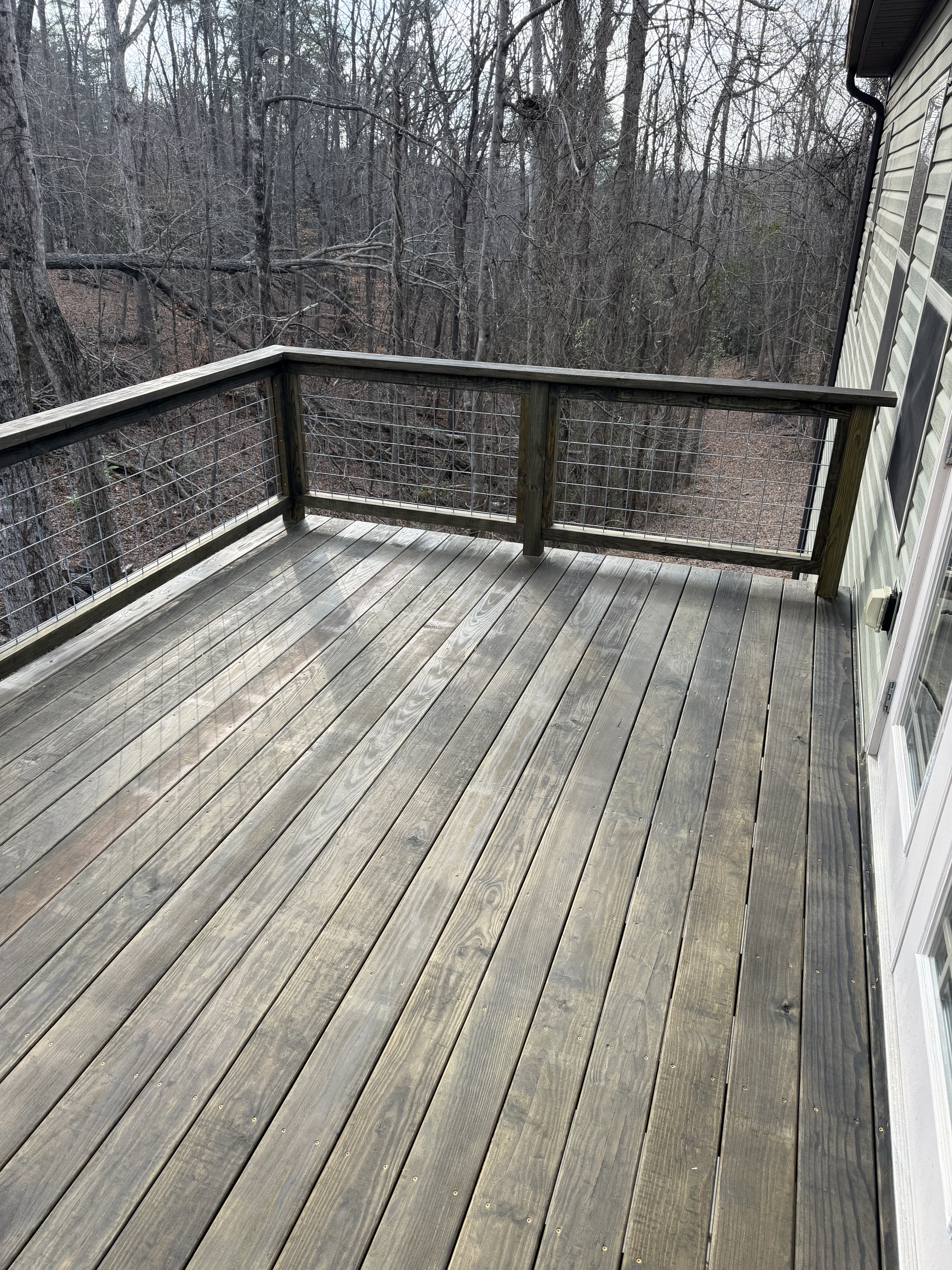 Completed Caleb deck with stained boards and hog-wire railing overlooking the wooded property