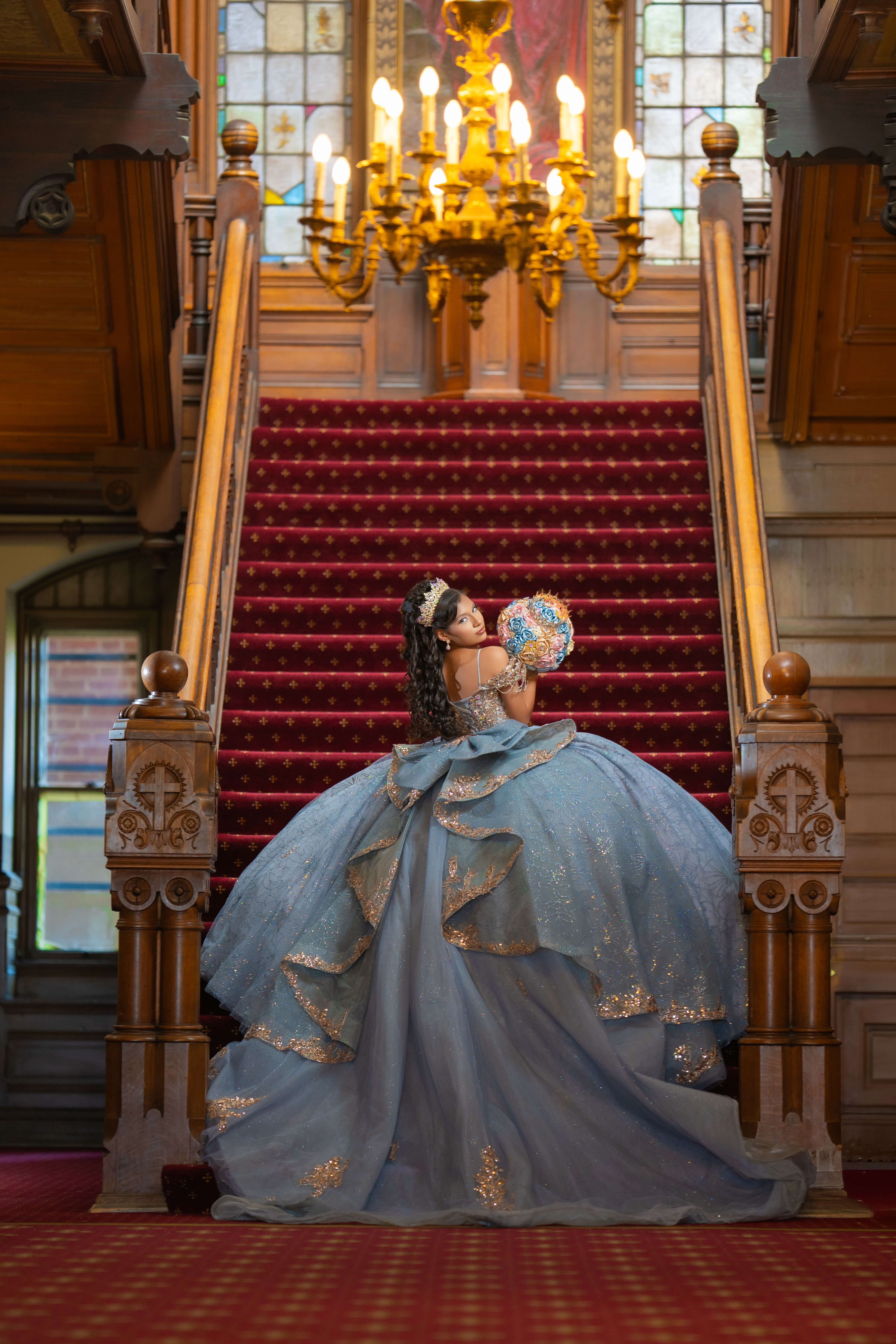 Quinceañera con vestido azul en una escalera con alfombra roja y candelabro