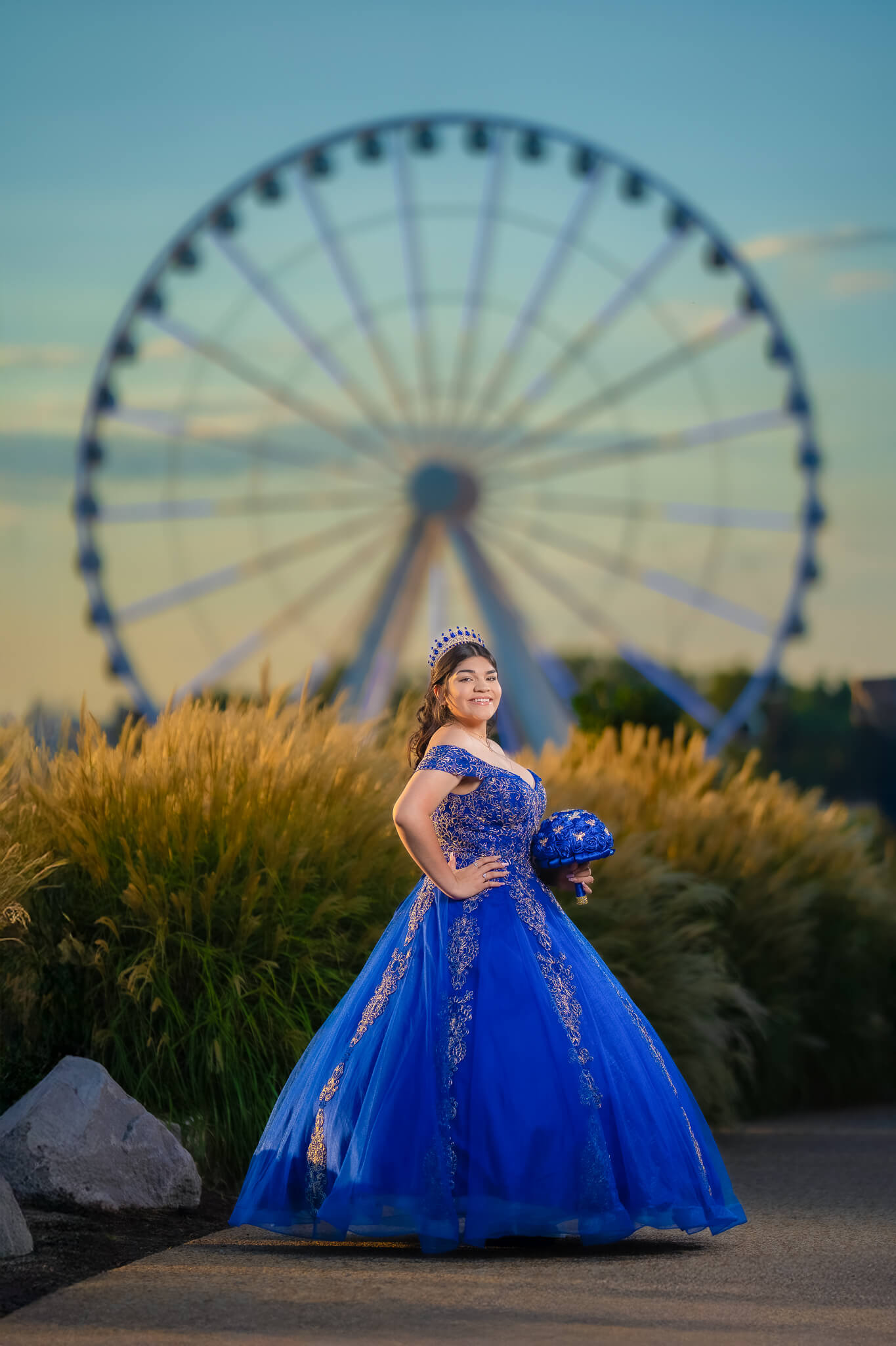 Quinceañera con vestido azul rey frente a una rueda de la fortuna iluminada