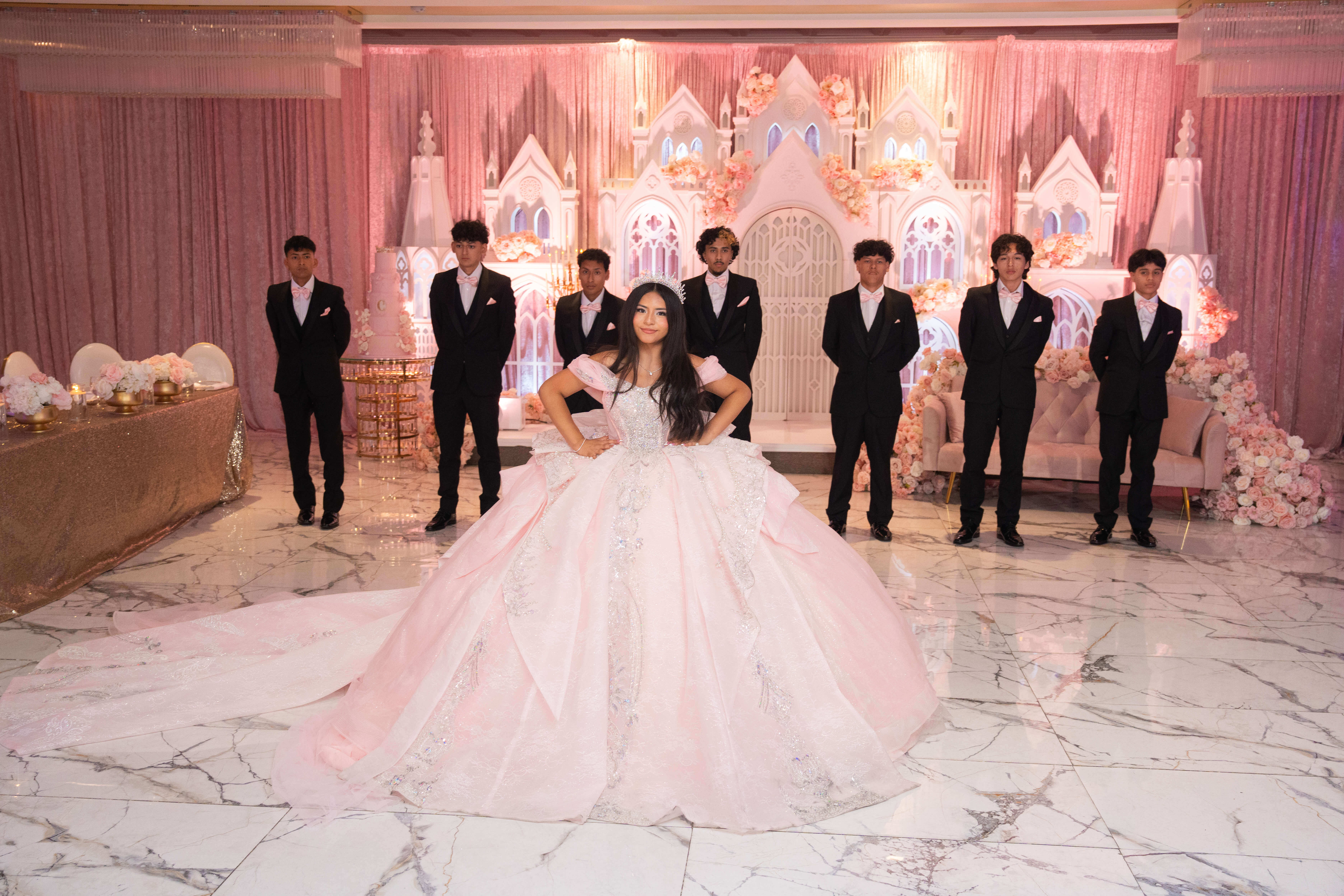 Quinceañera con vestido rosa al centro del salón junto a sus chambelanes