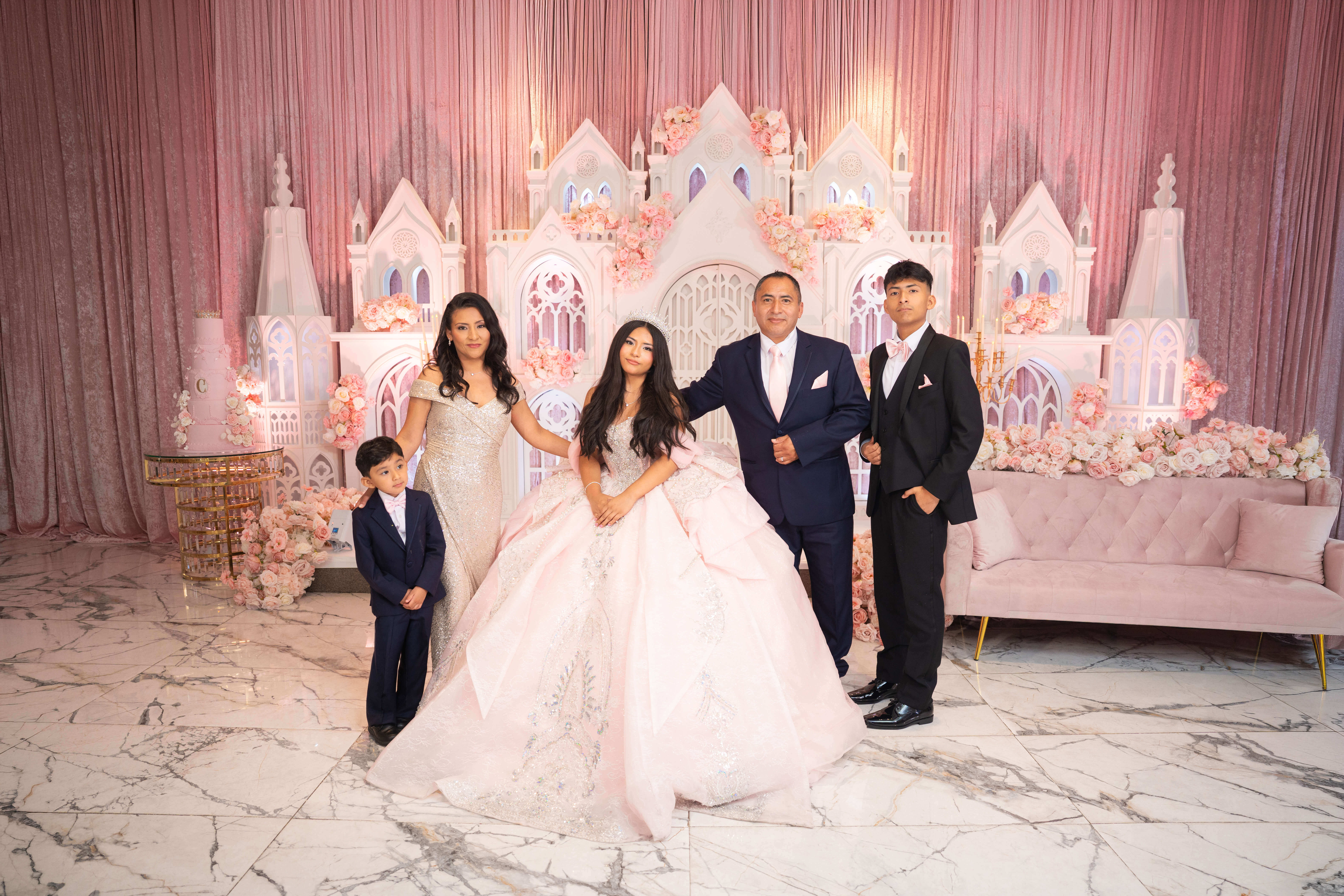 Quinceañera con sus papás y hermanos frente a la decoración del salón