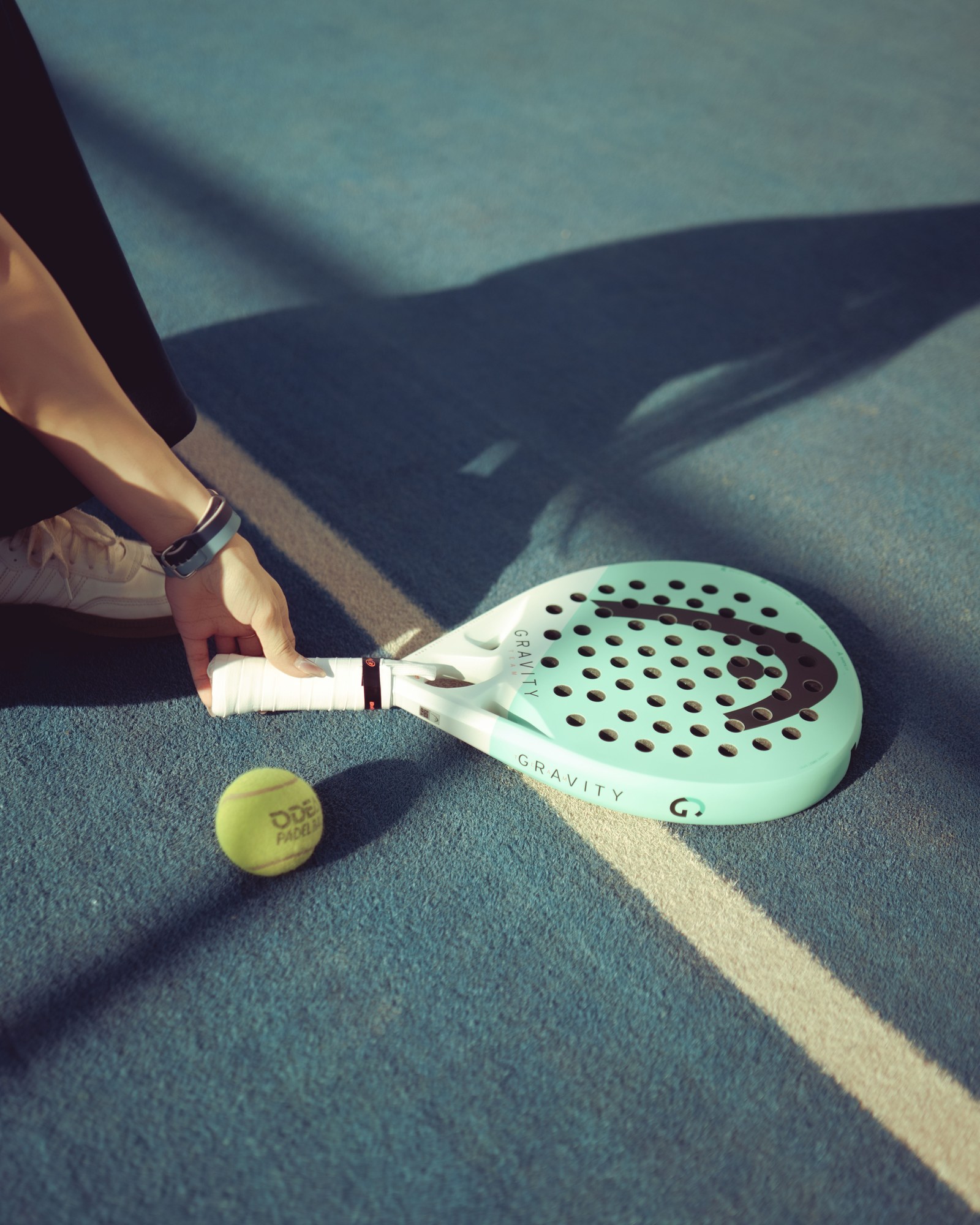 A player picking up a padel racquet and ball from a blue court