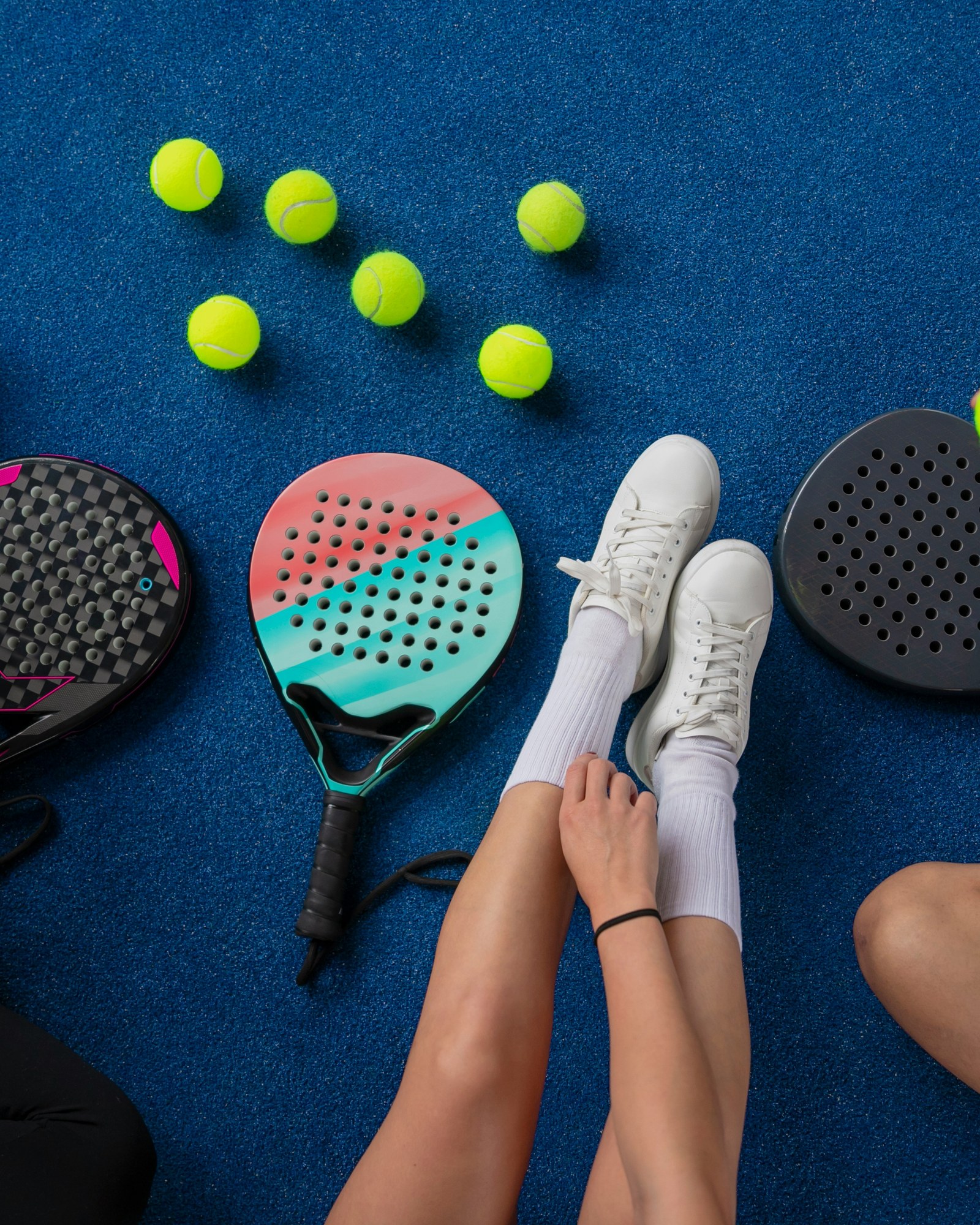 Friends sitting on a blue court with padel racquets and balls