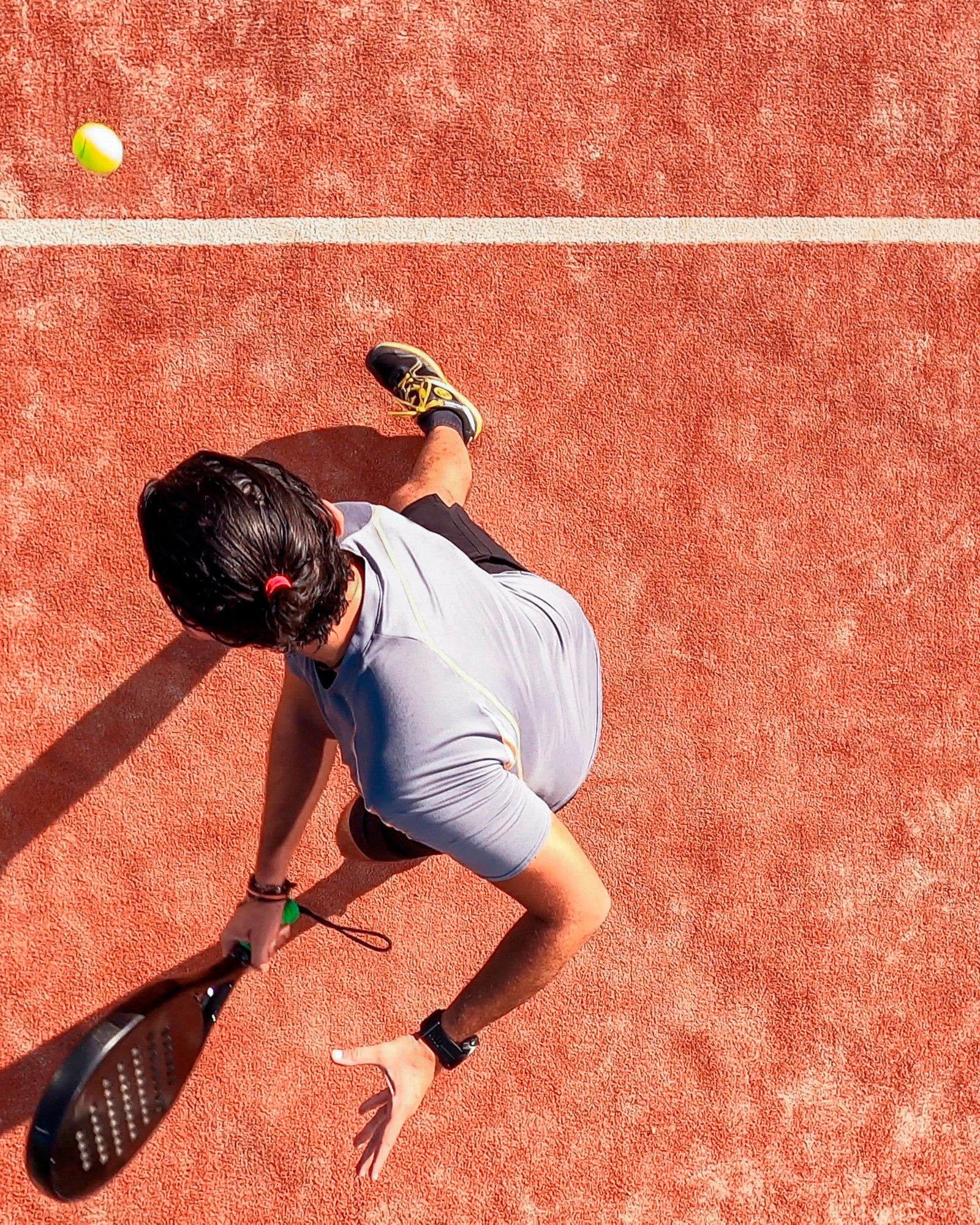 Overhead view of a player serving on an orange padel court