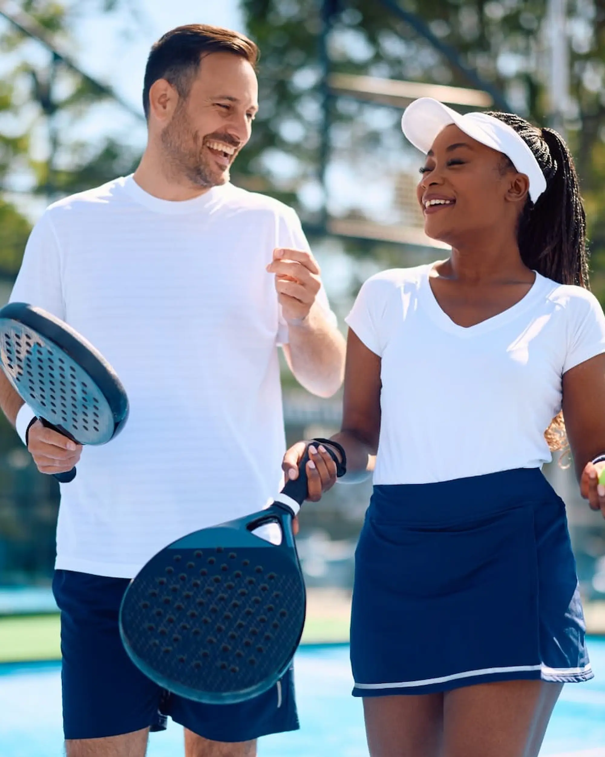A man and a woman walking together and laughing on an outdoor padel court
