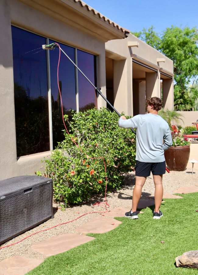 Caden cleaning exterior glass with a water-fed pole at a Valley home