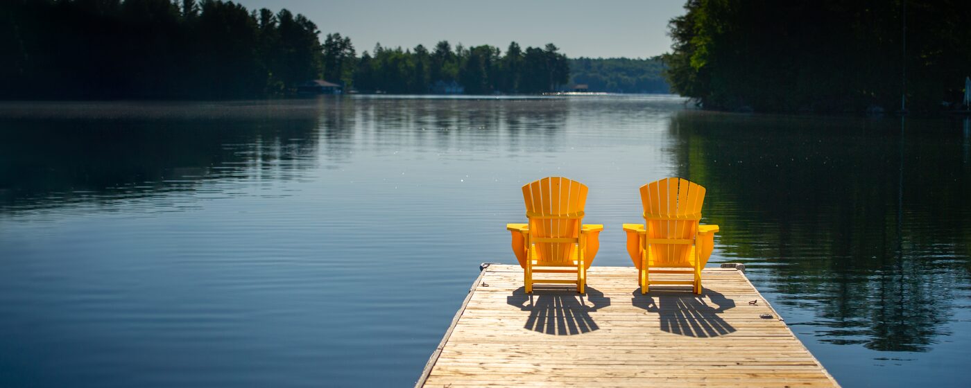 Two chairs side by side at the end of a dock, facing still water.