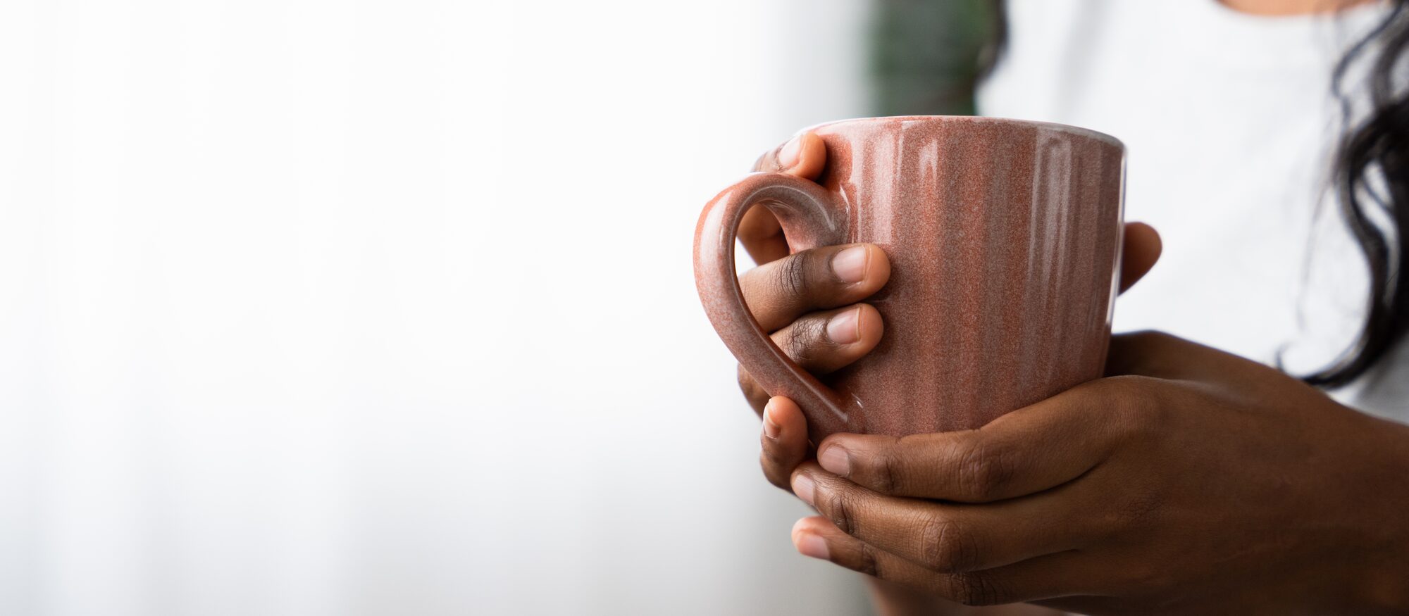 Two hands wrapped around a warm mug in soft daylight.