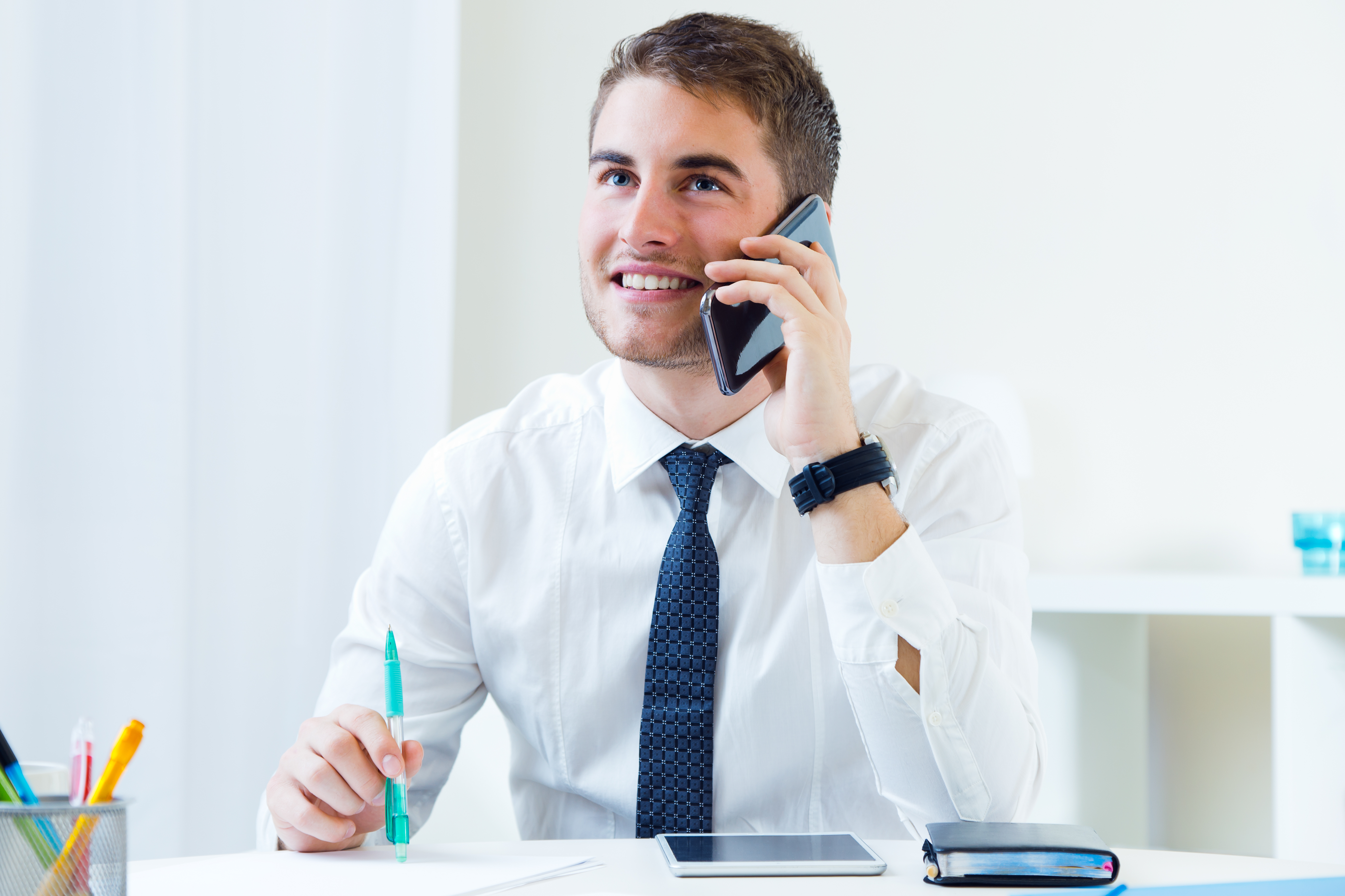 Man talking on phone and writing notes at desk.