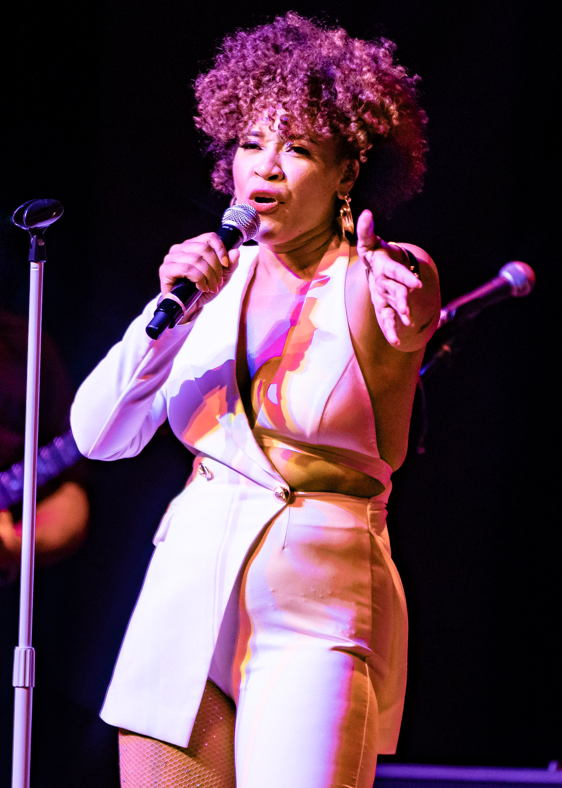 Tre’ Rochelle singing onstage in a white outfit, holding a microphone