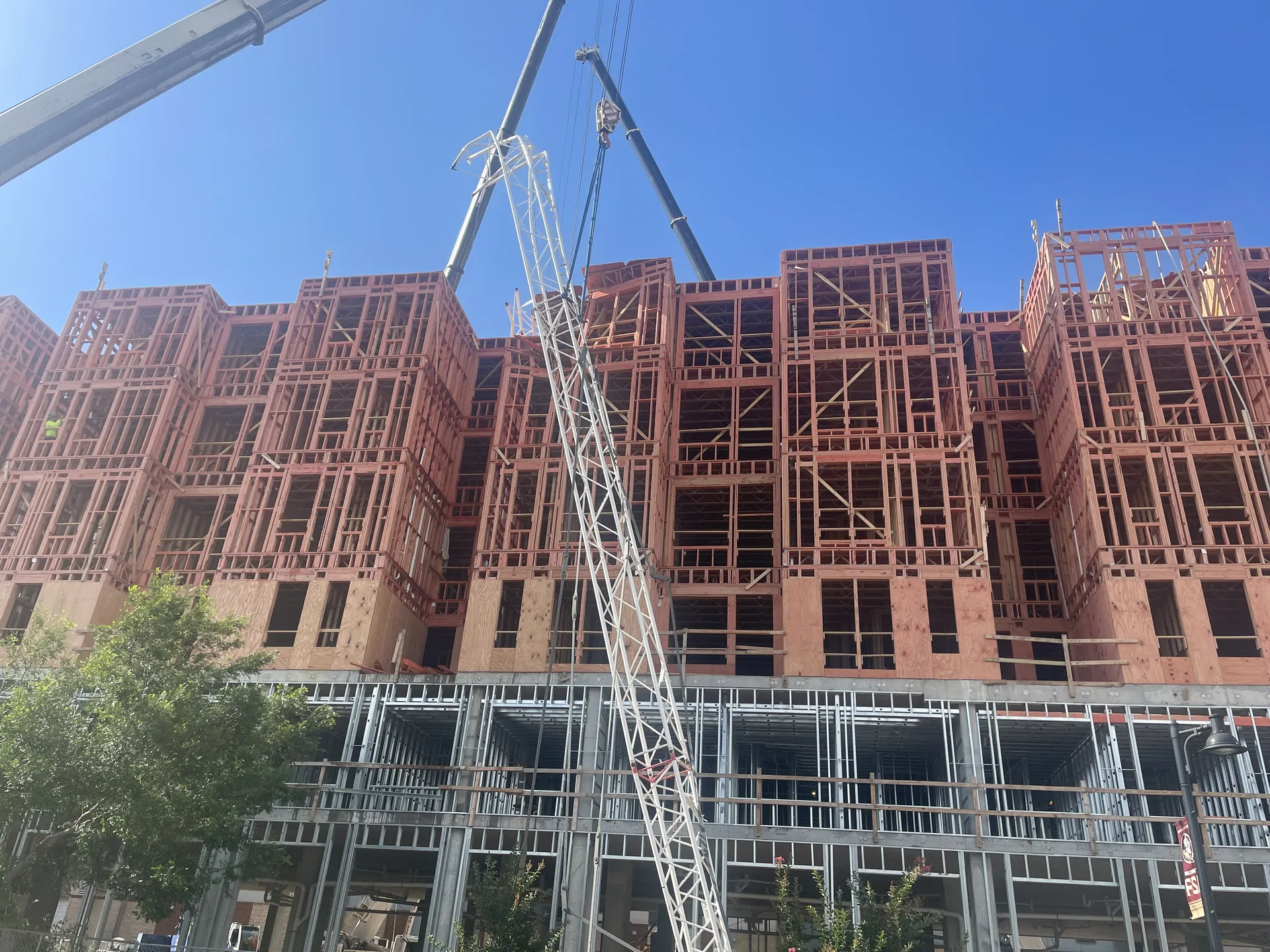 Multi-story wood framing rising above a steel and concrete podium, tower crane overhead