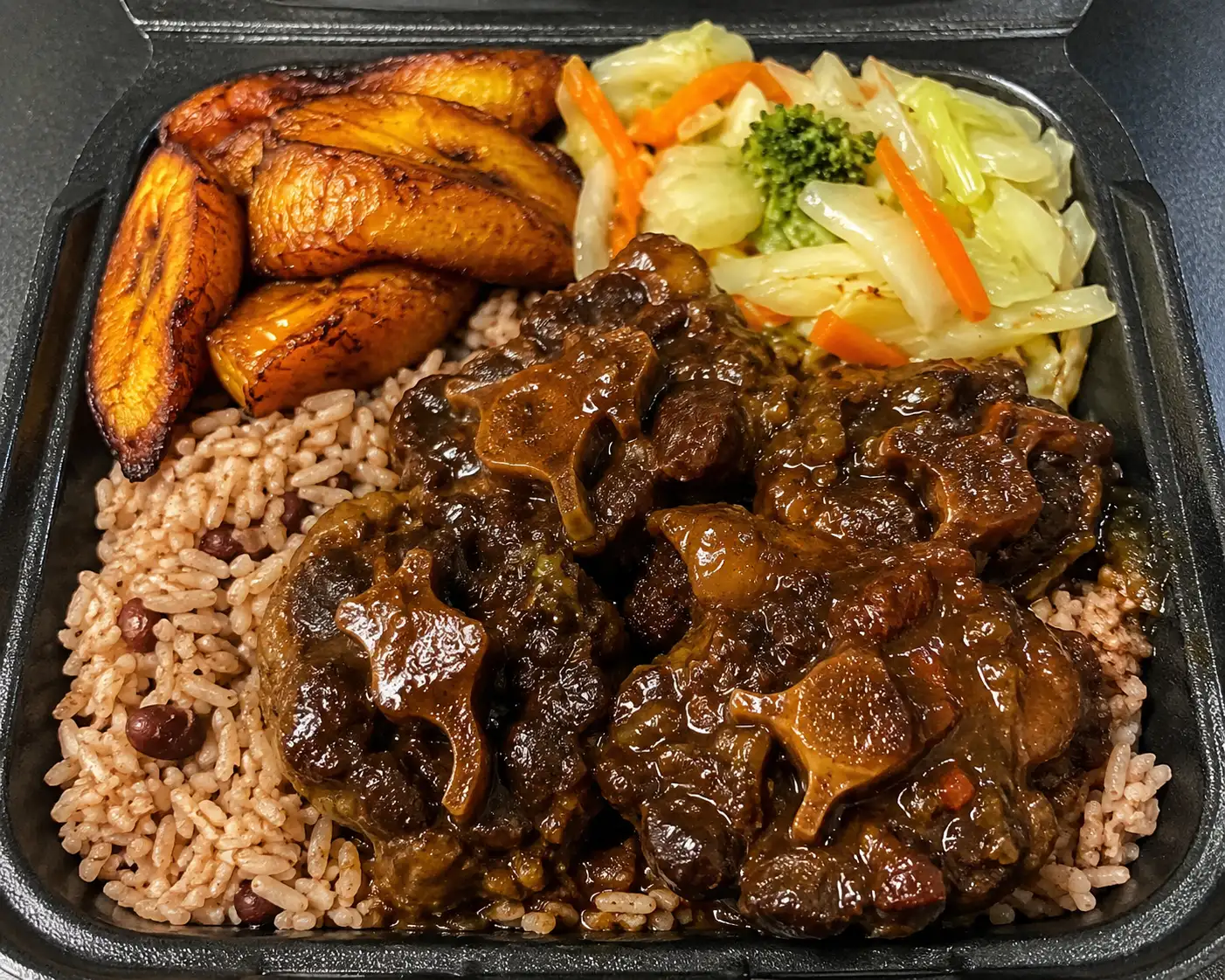 Oxtail dinner with rice and peas, fried plantains, and steamed cabbage