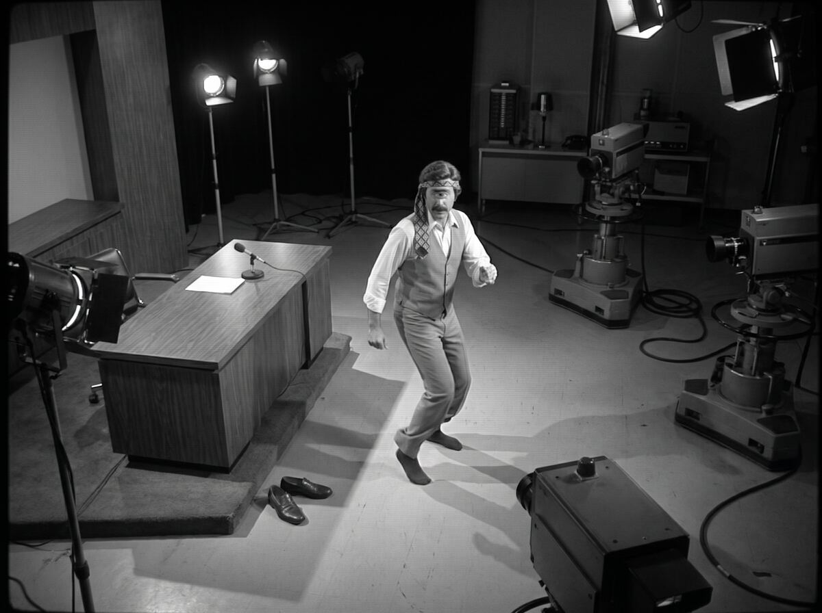 Black-and-white security camera view of Chet dancing alone in the empty studio