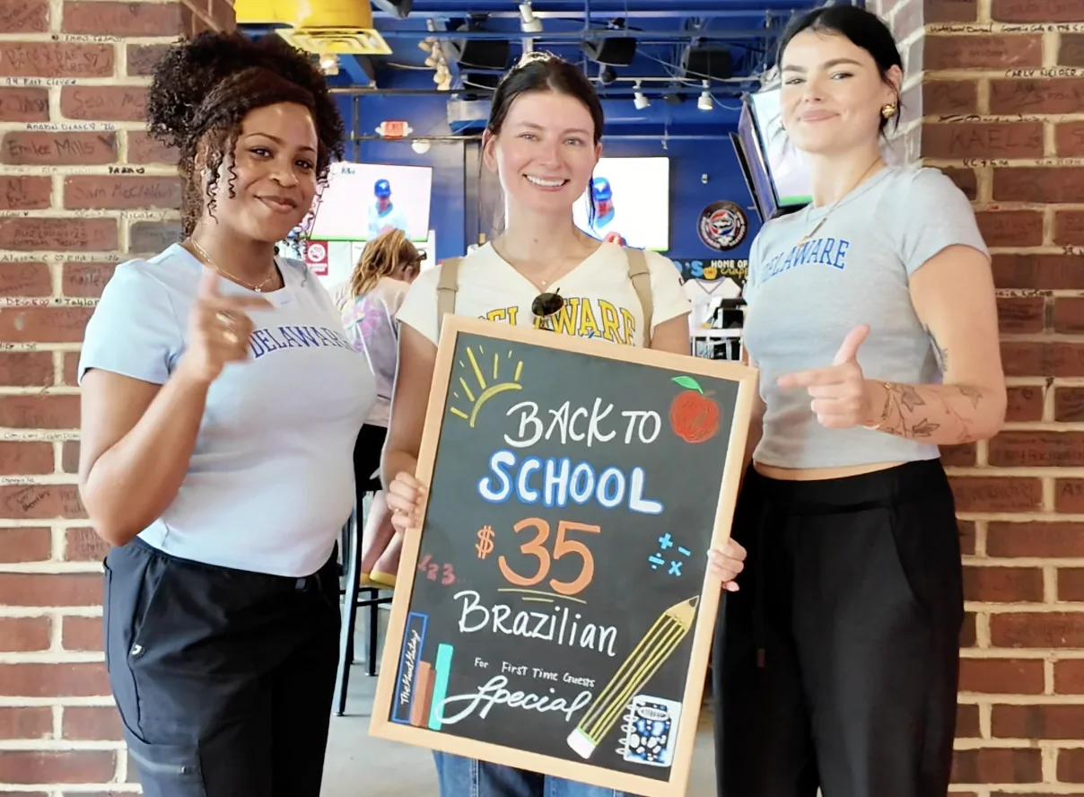Waxing The City team holding a chalkboard sign: Back to School $35 Brazilian for first-time guests