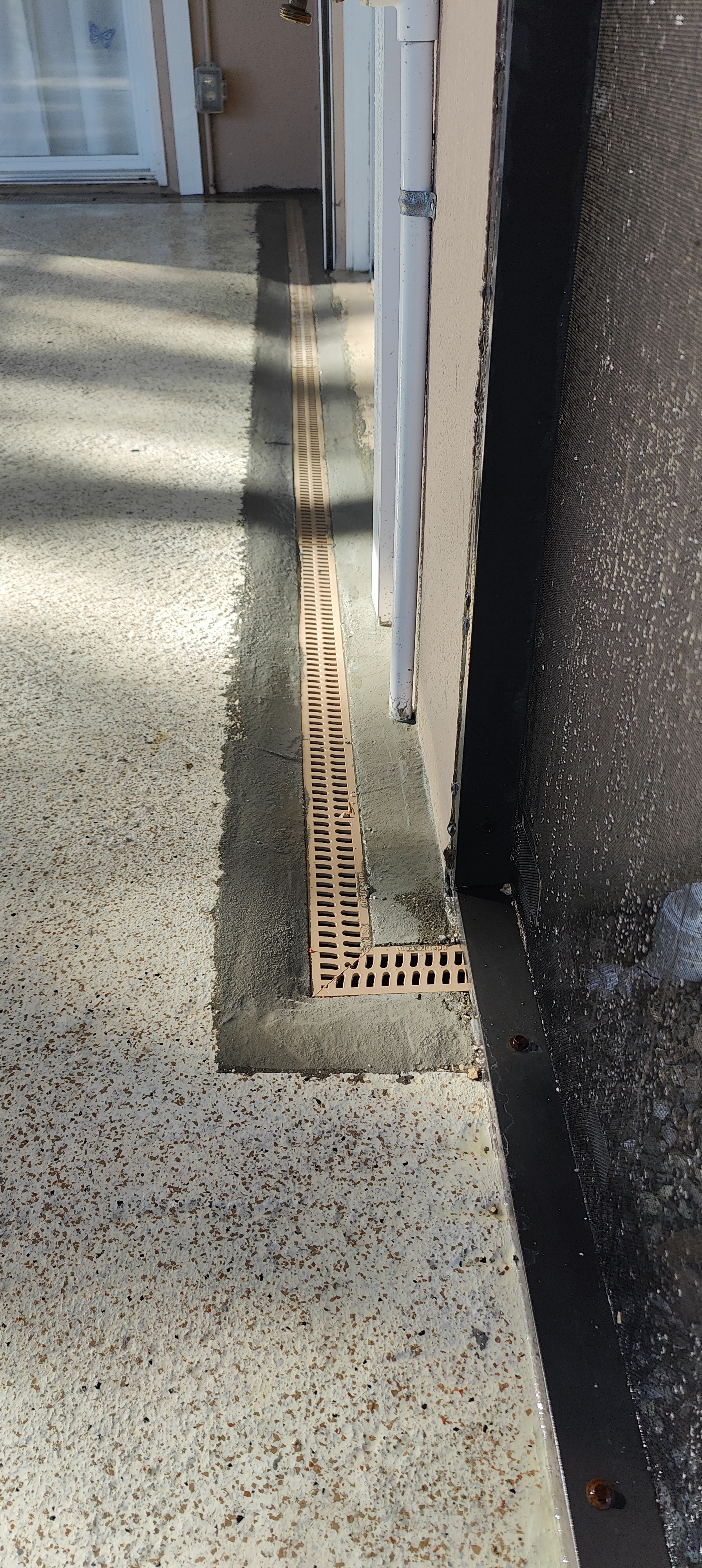 A finished Trufam channel drain with a tan grate set flush in a concrete driveway in Tampa Bay