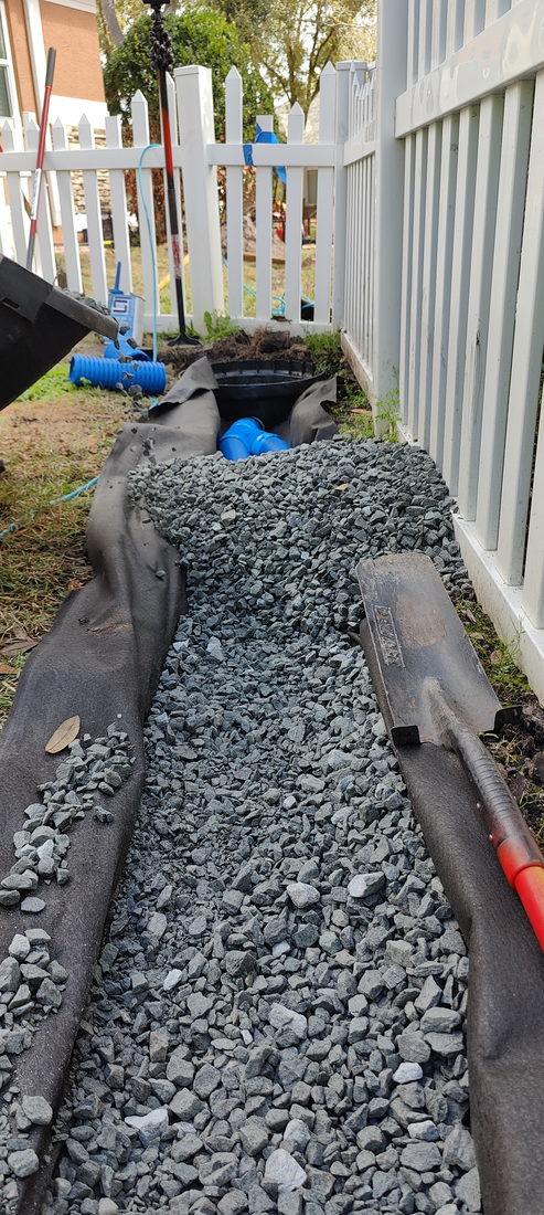 Open French drain trench lined with drainage fabric and filled with clean granite stone by Trufam Drainage