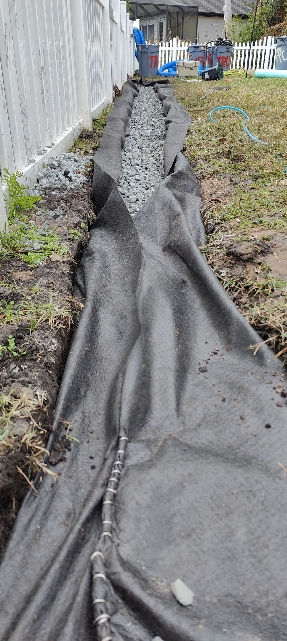 French drain installation in a Tampa Bay yard by Trufam Drainage with drainage fabric closing over the clean granite stone bed