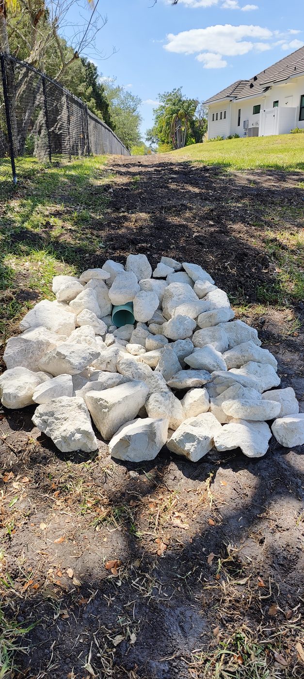 Finished underground drainage discharge outlet with a six inch main line daylighted into clean rip rap stone by Trufam Drainage