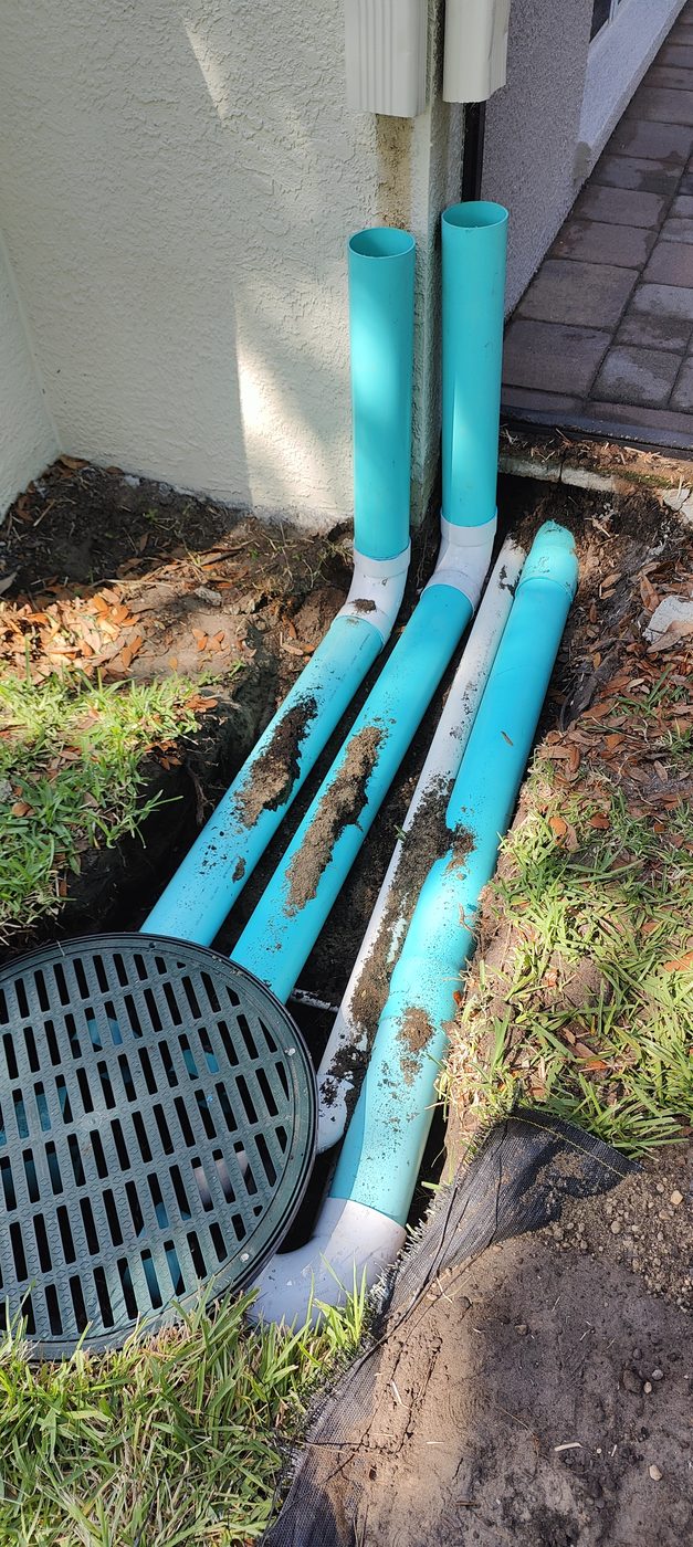 Trufam underground drainage system in Tampa Bay with solid SDR-35 downspout lines running into a grated distribution box beside the home