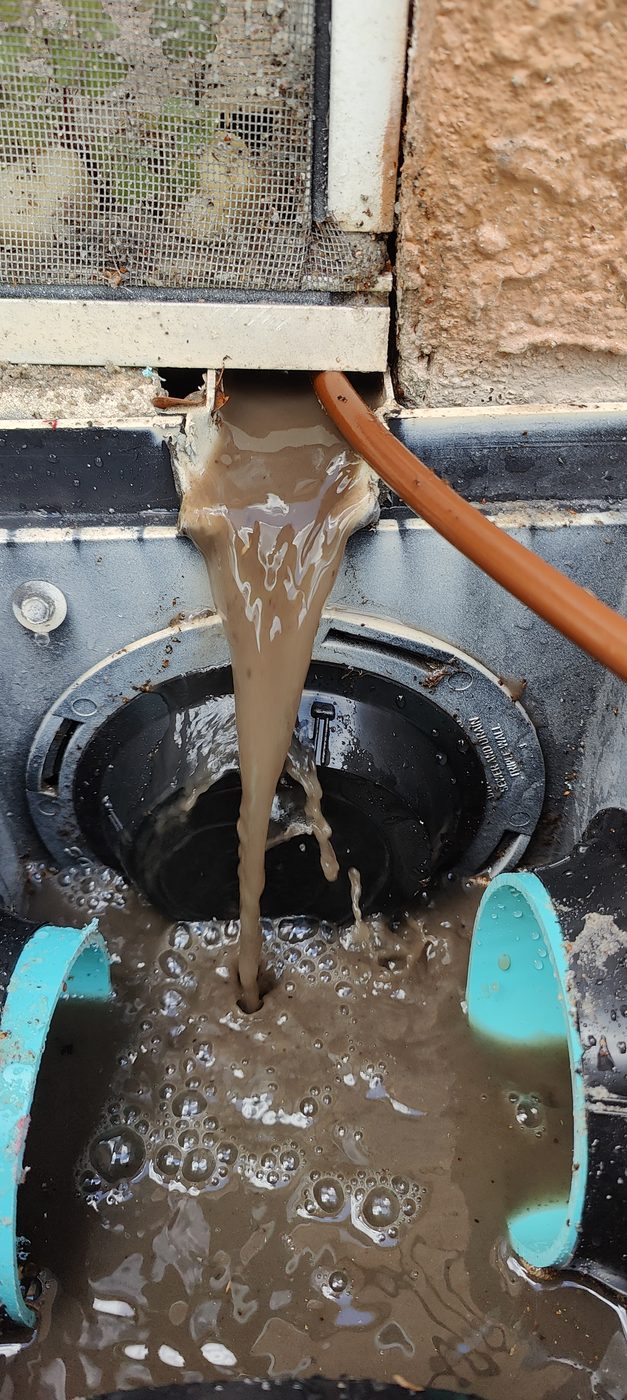 Muddy water and years of trapped sediment flushing out of a clogged underground drain line during a Trufam hydro jetting service in Tampa Bay
